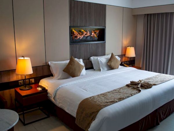 A cozy hotel room with a large bed, two lamps, decorative pillows, and a wall art piece, creating a warm and inviting atmosphere.