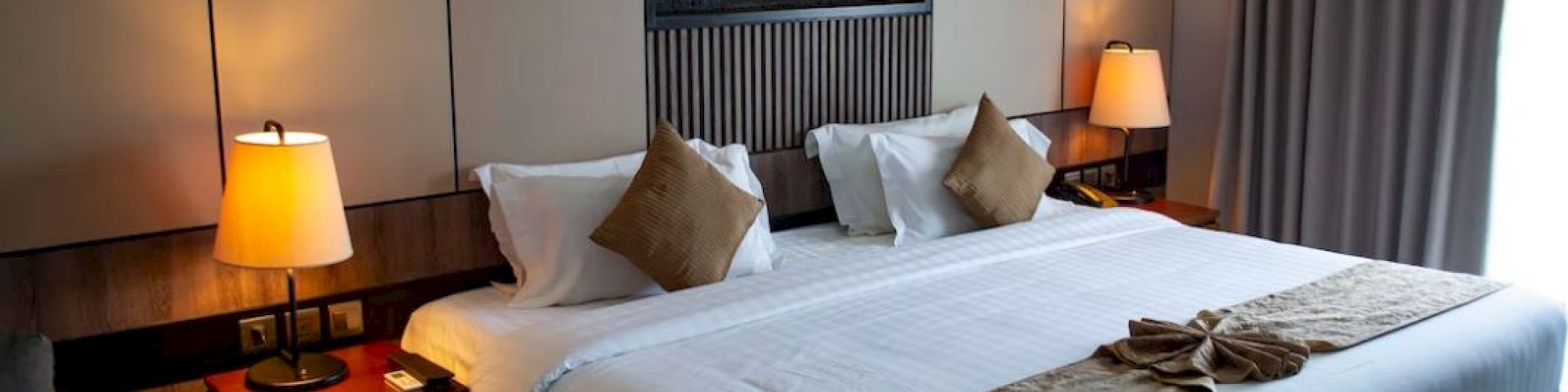 A cozy hotel room with a large bed, pillows, side tables with lamps, and a small decor feature above the headboard.