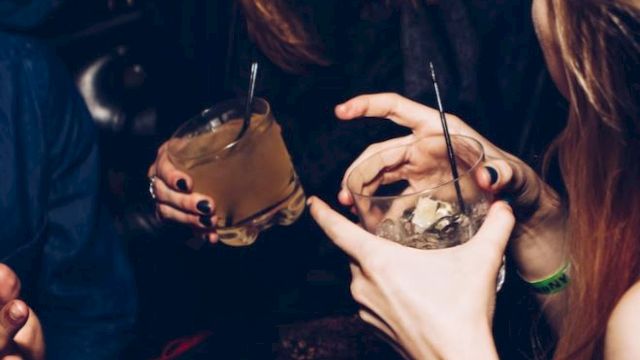 People are at a lively gathering, holding drinks and chatting.