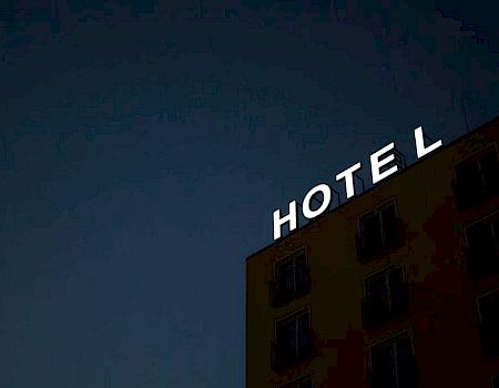 A building at night displays a sign saying "HOTEL" with the letter "L" not fully illuminated against a dark sky.