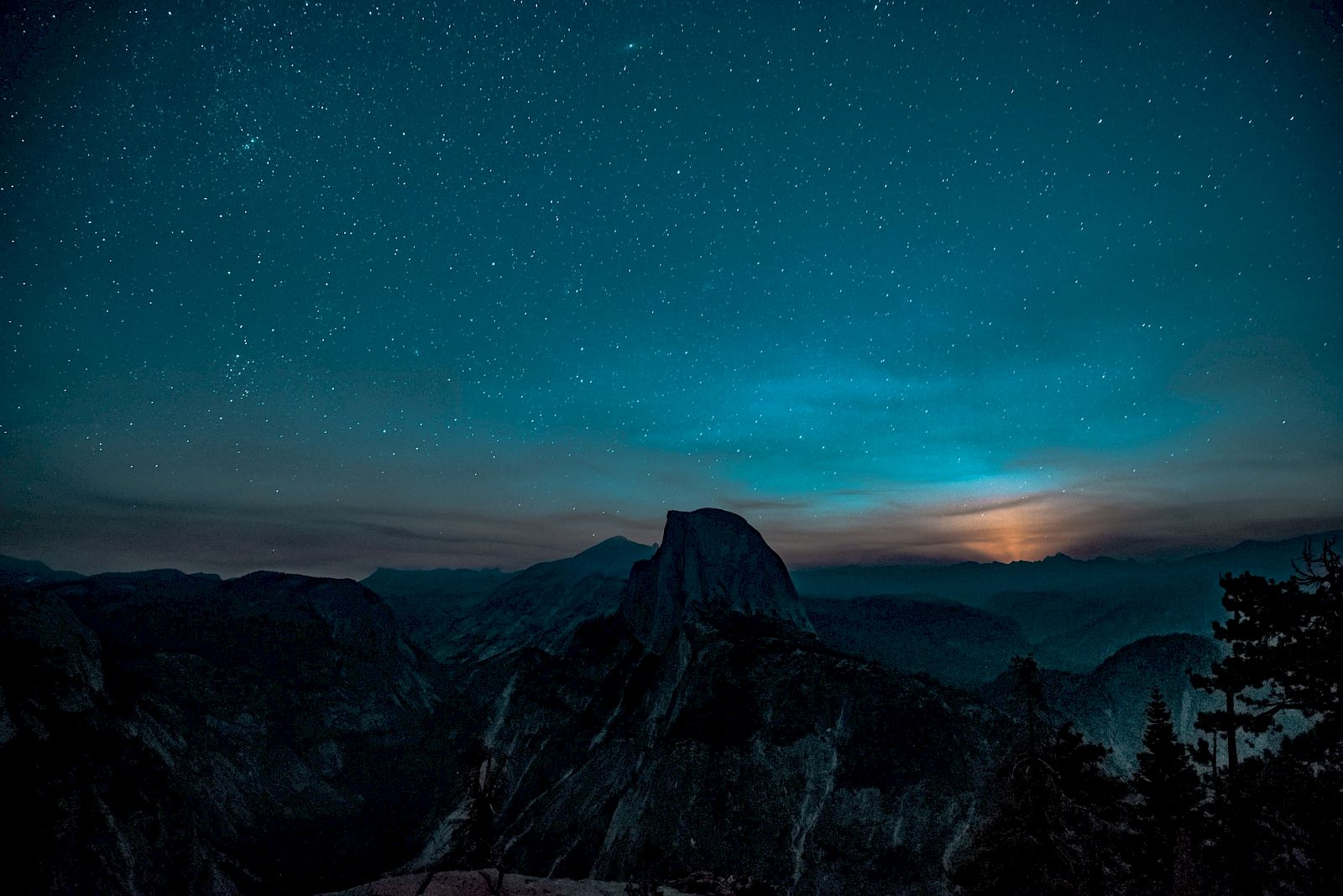 A silhouetted mountain under a starry night sky with a glow on the horizon, possibly from the moon or distant lights.
