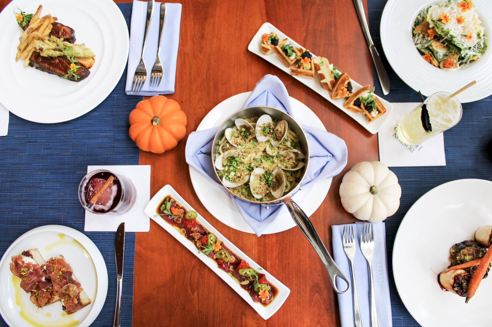 An elegant table setting with various dishes, including pasta, toast, salad, and drinks, adorned with small decorative pumpkins.