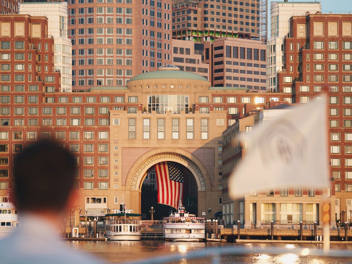 The image shows a patriotic scene with a large American flag hanging in a building archway, surrounded by cityscape and waterfront views.
