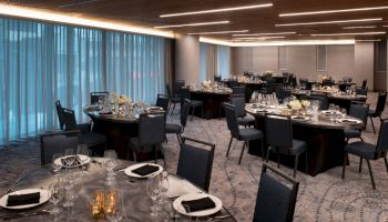 The image shows an elegantly set dining room with round tables, chairs, and dim lighting, suitable for a formal event or banquet.