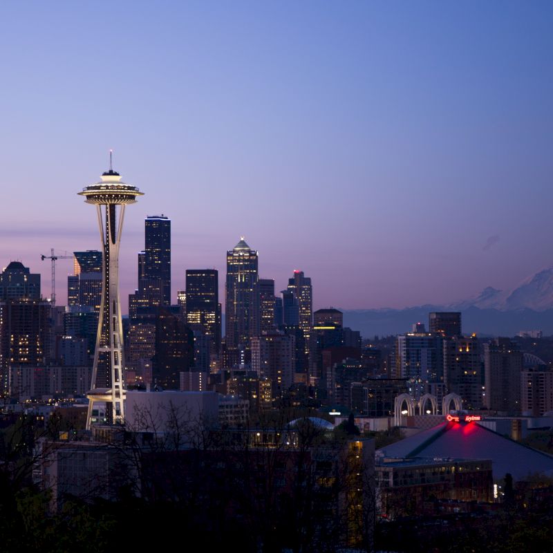 Seattle skyline at dusk featuring the Space Needle and Mount Rainier in the background.