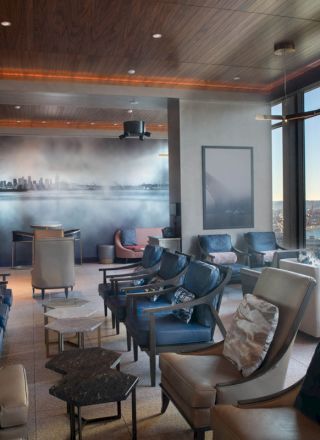 The image shows a modern lounge with leather chairs, a mural, large windows, and views of a waterfront and Ferris wheel, creating a cozy atmosphere.