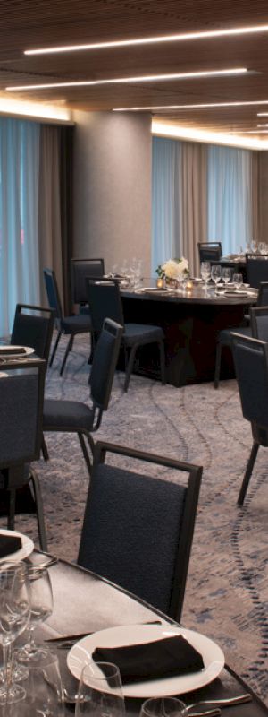 A banquet hall with round tables set for a formal event, featuring elegant tableware and decorations under soft lighting.