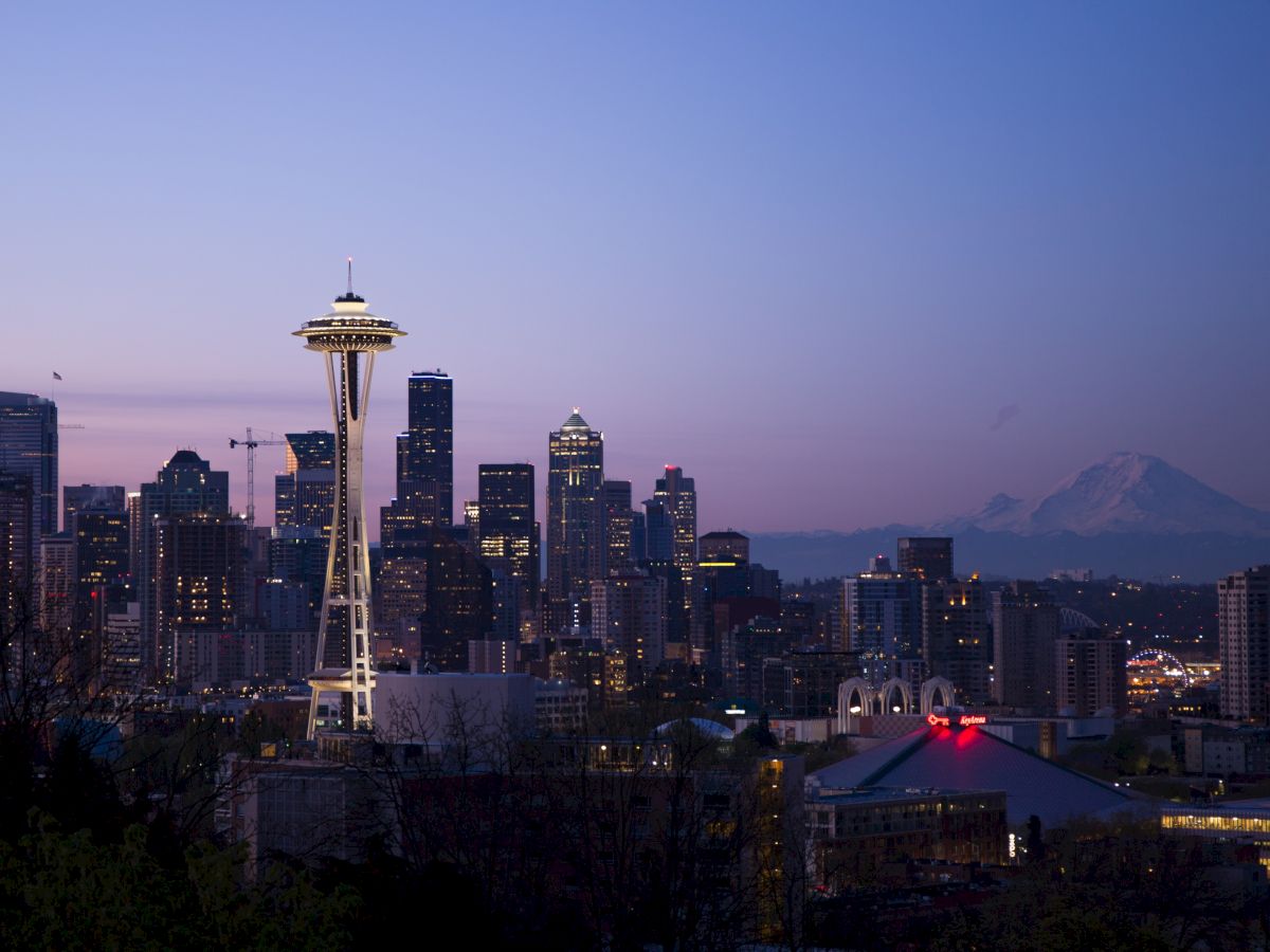 The image shows the Seattle skyline at dusk, featuring the Space Needle and city skyscrapers under a twilight sky with Mount Rainier in the background.