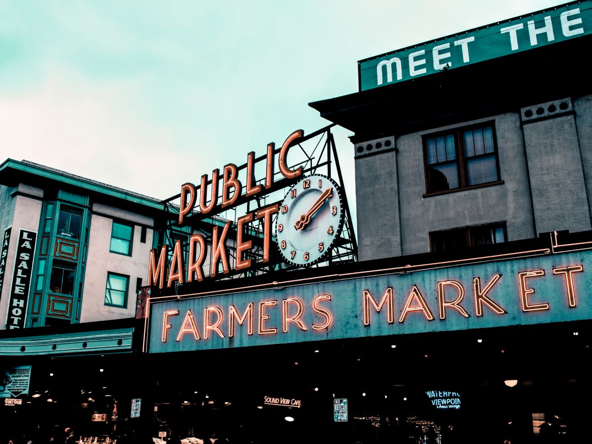 A vintage-style sign for a public farmers market with a clock, set against a building backdrop.