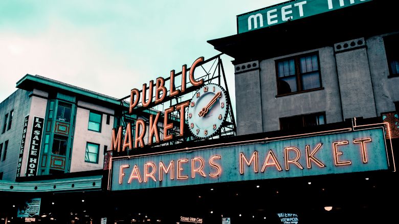 A vintage-style sign for a public farmers market with a clock, set against a building backdrop.